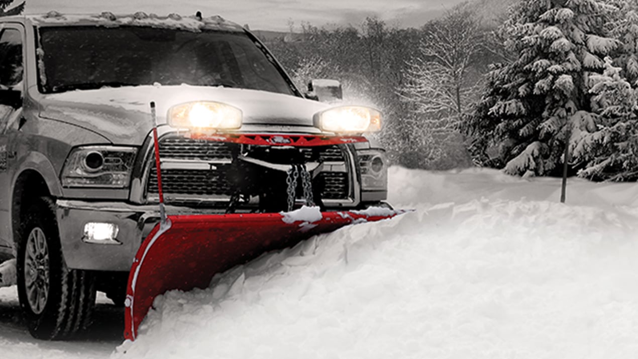 Truck with plow plowing a pile of snow with bright headlights
