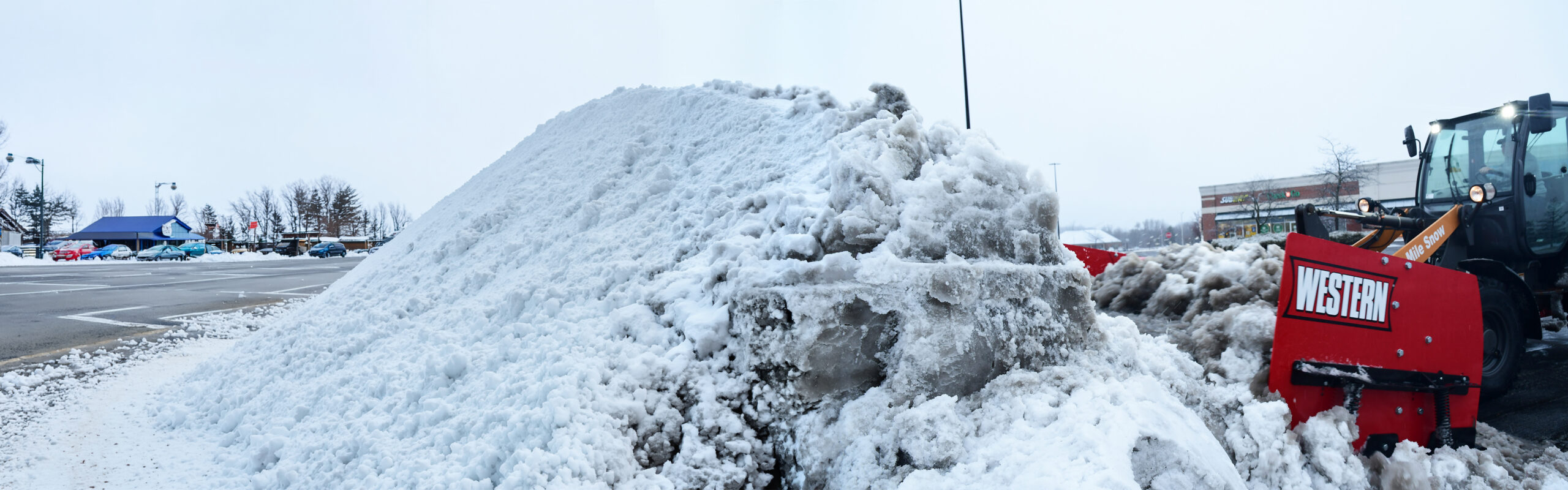 western pile driver pusher plow in parking lot with giant pile of snow